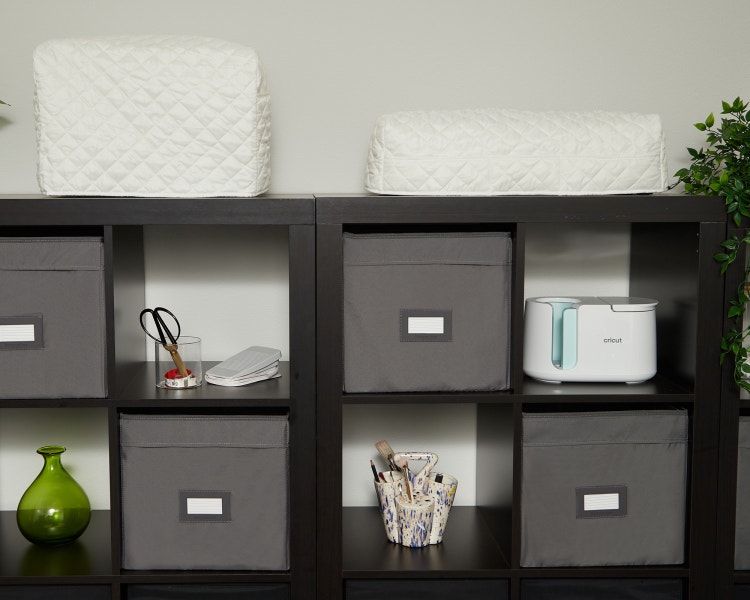 Organized craft room with cube storage bins and a covered sewing machine and cricut