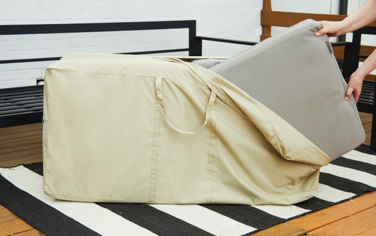 A pair of hands places outdoor cushions in a durable cushion storage bag.